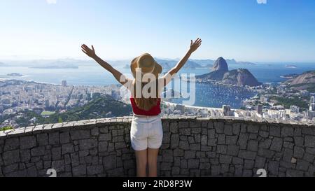 Urlaub in Rio de Janeiro. Wunderschönes, dankbares Traveler Girl mit erhobenen Armen und Blick auf Guanabara Bay mit Zuckerhut, UNESCO World He Stockfoto