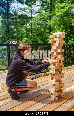 Ein Teenager, der mit einem großen Jenga-Turm in einer Hütte am See in Muskoka Ontario Kanada spielt Stockfoto