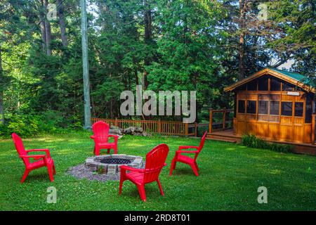 Vier rote Muskoka-Stühle um eine Feuerstelle in Muskoka Ontario Kanada Stockfoto