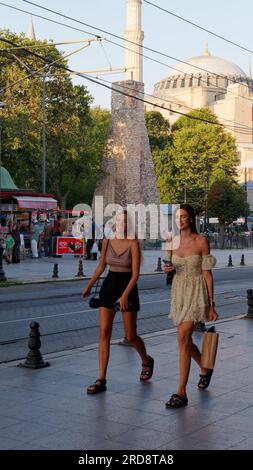 Zwei junge Frauen lächeln auf einer Straße in Sultanahmet an einem Sommerabend mit der Hagia Sophia Moschee dahinter, Istanbul, Türkei Stockfoto