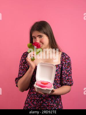 Glückliches Mädchen, das in die Kamera schaut, mit Bento-Kuchen und Blumen in der Hand hat Stockfoto