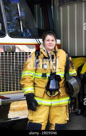 Attraktive Feuerwehrfrau steht vor dem Feuerwehrauto. Sie hält ihren Helm und die Gasmaske hängt um ihren Hals. Stockfoto