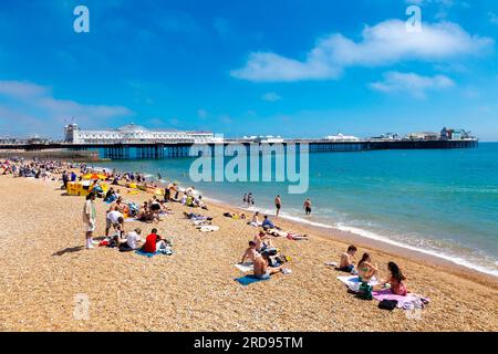 Leute, die an einem heißen Sommertag am Strand sitzen, mit Brighton Palace Pier im Hintergrund, Brighton, Großbritannien Stockfoto
