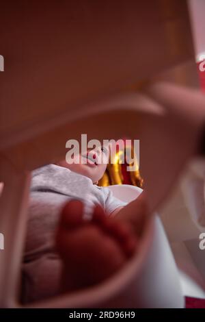 Ein Bild von unten von einem einjährigen Jungen mit festlichem Hut sitzt auf einem Kinderstuhl mit Stofffahnen. Kind auf isoliertem roten Hintergrund mit Foliengold Stockfoto