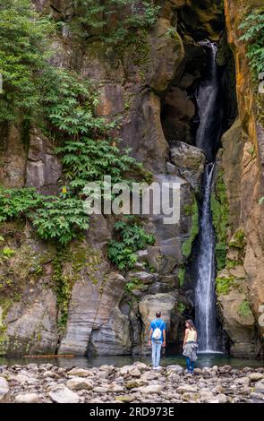 Ribeira Grande, Azoren - 05.09.2019: Ein paar Touristen stehen in der Nähe des wunderschönen Wasserfalls „Salto do Cabrito“. Die Insel Sao Miguel auf den Azoren Stockfoto