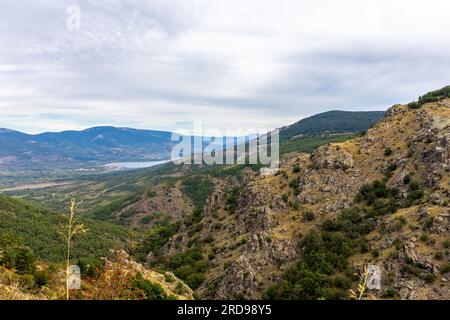 Felsige Berge im zentralen System in Spanien, Landschaft mit Pinilla del Valle Dorf und Pinilla Reservoir in der Ferne, Blick von der M-611 Straße. Stockfoto