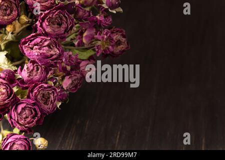 Strauß trockener rosafarbener Rosen auf dunklem Holzhintergrund, Nahaufnahme. Begriff der Einsamkeit oder des Alters. Traurigkeit, unglückliche Liebe. Stockfoto