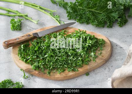 Holzbrett aus gehacktem Grünkohl und Küchenmesser auf grauem, strukturiertem Hintergrund. Kochen Sie eine köstliche, gesunde Mahlzeit. Stockfoto