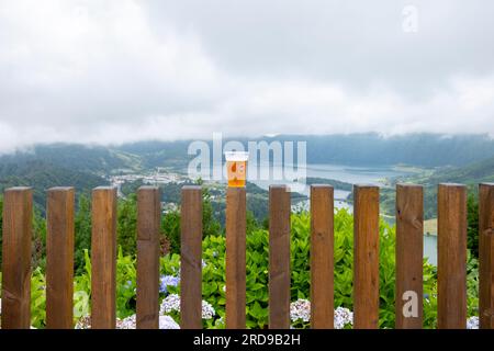 São Miguel, Azoren - 27.07.2019 Uhr: Ein Glas "Super Book - Sabor Autentico" auf einem Holzzaun mit Blick auf den See "Lagoa das Sete CI" in den sieben Städten Stockfoto