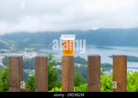 São Miguel, Azoren - 27.07.2019 Uhr: Ein Glas "Super Book - Sabor Autêntico" auf einem Holzzaun mit Blick auf den See "Lagoa das Sete CI" in den sieben Städten Stockfoto