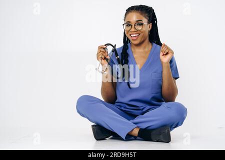 Porträt einer lächelnden Krankenschwester oder Ärztin in blauen Bürsten Uniform sitzendes Stethoskop Stockfoto
