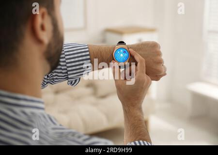 Mann stellt Smart-Home-Steuerungssystem über Smartwatch in Innenräumen ein, Nahaufnahme. App-Oberfläche mit Symbolen auf dem Display Stockfoto