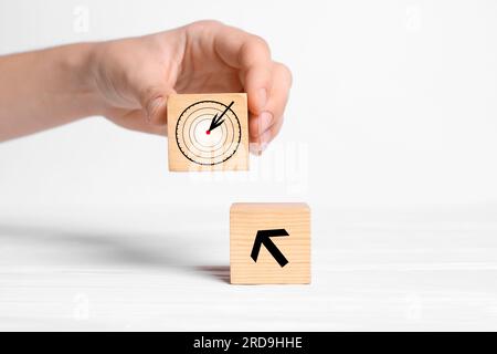 Eine Frau, die einen Würfel mit einem Zielsymbol auf weißem Hintergrund platziert, Nahaufnahme Stockfoto