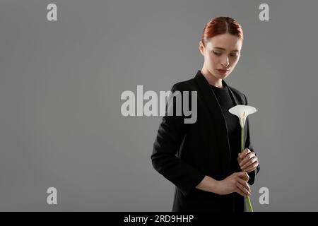 Traurige Frau mit Calla-Lilienblume auf grauem Hintergrund, Platz für Text. Beerdigungszeremonie Stockfoto