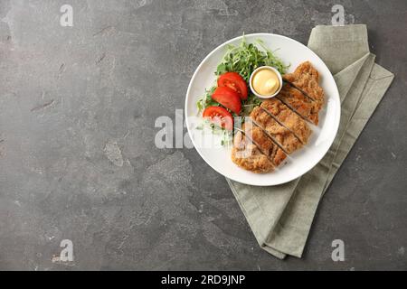 Leckeres Schnitzel serviert mit Sauce, Microgreens und Tomate auf einem grauen strukturierten Tisch, Draufsicht. Platz für Text Stockfoto