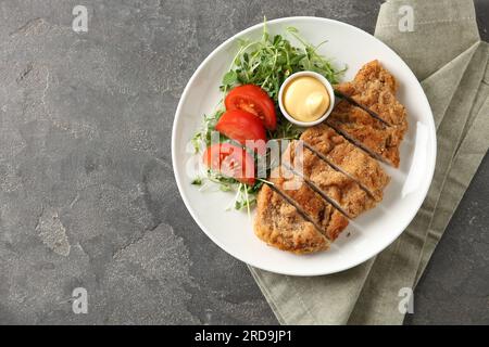 Leckeres Schnitzel serviert mit Sauce, Microgreens und Tomate auf einem grauen strukturierten Tisch, Draufsicht. Platz für Text Stockfoto