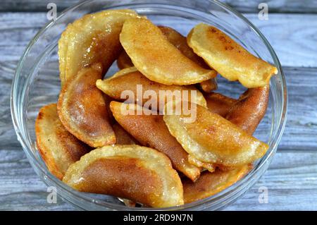 Eine Schüssel mit Qatayef-Knödeln gefüllt und gefüllt mit Nüssen und zerkleinerten Kokosnüssen, in tiefem Öl gebraten und mit Zuckersirup getränkt, arabischer Dessert gefaltet Pfanne Stockfoto