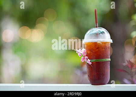 Plastikkaffeetasse, gefrorener Americano (schwarzer Kaffee) auf einem Holztisch im Garten Stockfoto