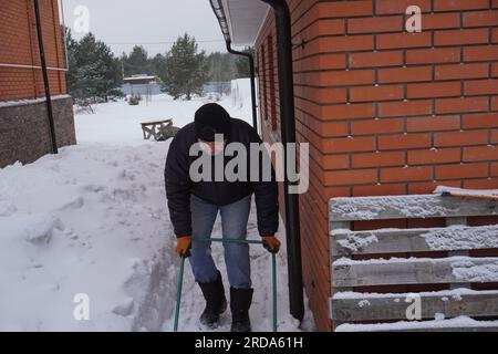 Ein Mann reinigt im Winter Schnee im Hof des Hauses. Ein Mann reinigt den Schnee mit einer Schaufel Stockfoto