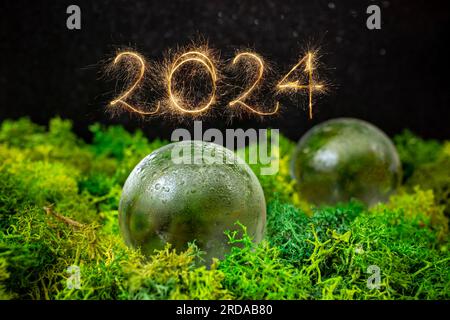 2024-Nummer mit goldenen Funkeln neben Glaskugeln auf grünem Flechten mit schwarzem Hintergrund und weicher Nahaufnahme Stockfoto