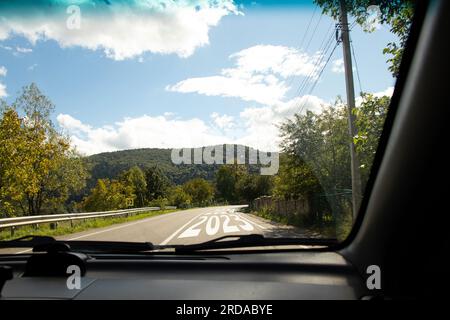 Blick aus dem Auto auf der Straße, wo 2023 und 2024 auf der Straße zu den Karpaten in der Ukraine geschrieben sind, die Straße mit einer Kurve und dem Anfang von a n Stockfoto