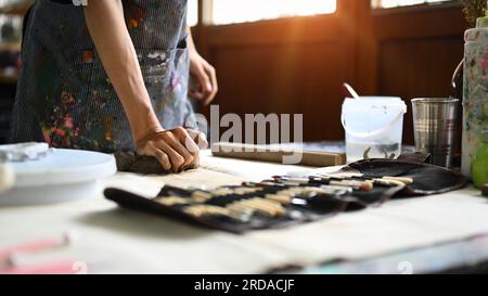 Töpferkünstler im Schürzenkneten von rohem Ton auf Holztisch. Handwerk, Kreativität, Hobby und Aktivitätskonzept Stockfoto