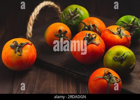 Sammlung von ganzen farbigen Tomaten, serviert auf einem rustikalen Holzhintergrund, Tomaten sind noch lebendig Stockfoto