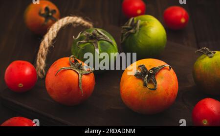 Sammlung von ganzen farbigen Tomaten, serviert auf einem rustikalen Holzhintergrund, Tomaten sind noch lebendig Stockfoto