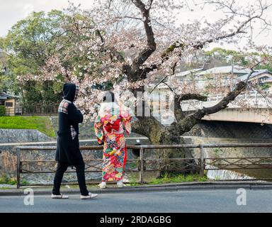 Junge Frau im traditionellen Stil des japanischen Kimonos, die Fotos mit dem Smartphone macht. Spaziergang entlang des Kamo River in der Präfektur Kyoto. Japan. Stockfoto