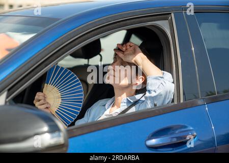 Erschöpfte Frau mittleren Alters fährt Autowellen blauer Fan leidet an Stau im Verkehr. Stockfoto