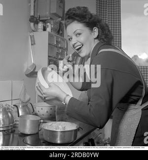 In der Küche im 1950er. Jahrhundert. Eine junge Frau in der Küche, die einen Kuchen macht. Sie schmeckt den Kuchenteig, wie man ihn beim Backen schmeckt. Sie ist die Schauspielerin Marion Sundh, 1927-1987, abgebildet in einem "zu Hause" Bericht 1951. Conard Ref. 1689 Stockfoto