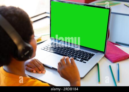 Ein birassistischer Junge mit Kopfhörern, der online über einen Laptop zu Hause auf dem Tisch lernt, Kopierraum Stockfoto