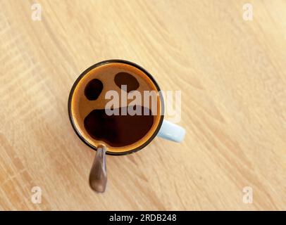 Kaffeetasse mit lustigem Schreien im Angstgesicht, Draufsicht. Öffnen Sie den weinenden Mund in der Tasse auf dem Tischhintergrund. Schockiert, gestresst, wütend, verängstigt und wütend Stockfoto