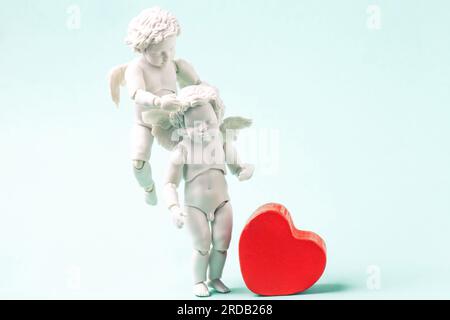 Engelsbaby und rotes Herz auf blauem Hintergrund. Weiße, kleine Amis, die am Himmel fliegen, altmodischer Stil. Süße Valentinstag-Begrüßung mit Engelchen-Figuren Stockfoto