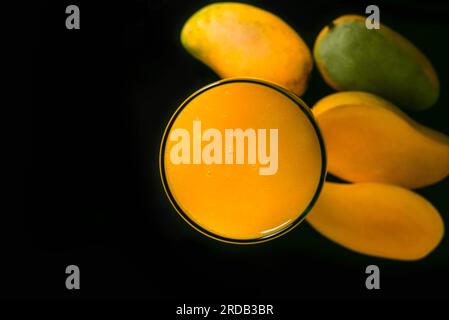 Mangosaftglas und eine Gruppe Mangos auf einem schwarzen Glastisch. Blauer Hintergrund. Draufsicht. Stockfoto