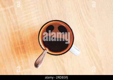 Pareidolie. Kaffeetasse mit lustigem Schrei im Angstgesicht, Draufsicht. Mund auf, Augen in Tasse auf dem Tisch. Schockiert, gestresst, wütend, beängstigend, wütender Schaum Stockfoto