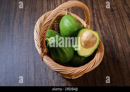 Korb mit Avocados auf Holztisch. Korb mit Avocados und einer Avocado in zwei Hälften geschnitten. Stockfoto