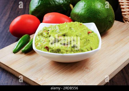 Guacamole wird auf einem weißen Teller auf einem Holztisch serviert. Guacamole Zutaten. Stockfoto