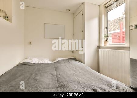 Ein Bett in einem Zimmer mit Fenster und Klimaanlage an der Wand neben dem Bett ist eine elektrische Heizung Stockfoto