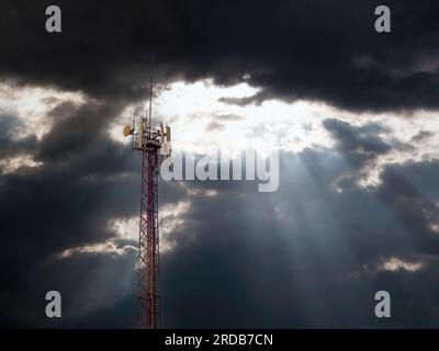 Mobile Antenne, hoher Metallturm vor einem dramatischen Himmel mit den Sonnenstrahlen, die durch die Wolken brechen. Stockfoto