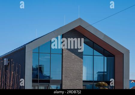 Ein modernes Haus im architektonischen Stil eines Scheunenhauses. Die Fassade ist grau, mit Stahl und Ziegeln und großen Fenstern dekoriert Stockfoto