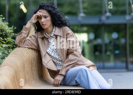 Depressive Erwachsene Frau, die auf einer Bank vor dem Bürogebäude sitzt, Geschäftsfrau Chefin, die verärgert und enttäuscht über die Ergebnisse von Erfolgen bei der Arbeit, Bankrott und finanzielle Verluste Wirtschaftskrise. Stockfoto