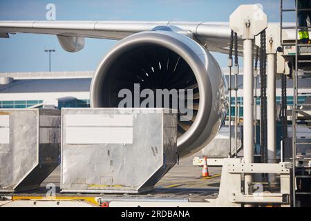 Vorbereitung des Flugzeugs am Flughafen. Verladung von Frachtcontainern in das Flugzeug. Selektiver Fokus auf großen Düsentriebwerk. Stockfoto