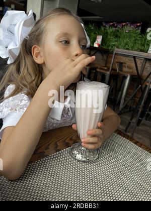 Schulmädchen mit Schleifen trinkt einen Milchshake Stockfoto