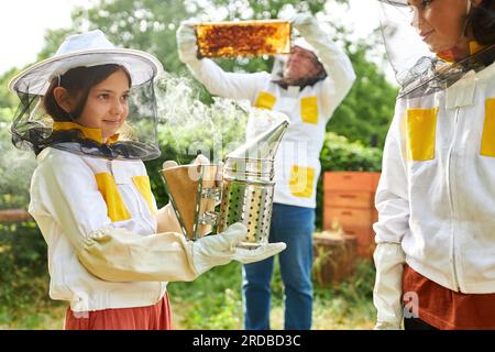 Lächelnde Mädchen mit Raucher, die neben einem männlichen Imker stehen und Wabenrahmen im Garten halten Stockfoto