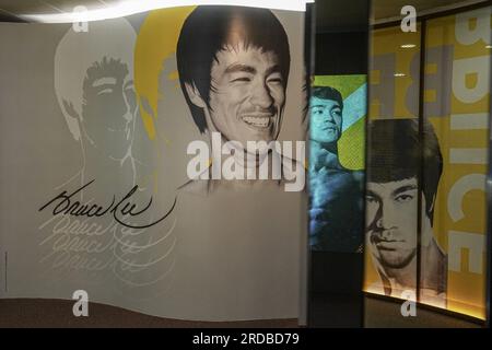 Riesige Poster von Bruce Lee sind in der Ausstellung zu sehen. Die Regierung Hongkongs feiert den 50. Todestag des Kampfkünstlers Bruce Lee mit einer bedeutenden Ausstellung im Hong Kong Heritage Museum. Die Ausstellung zieht Hunderte von Besuchern an und zollt dem Leben und Vermächtnis des legendären Kampfkünstlers Tribut und fasziniert die Besucher mit Ausstellungen, die seine außergewöhnlichen Leistungen und seinen kulturellen Einfluss zeigen. Gleichzeitig gehen einige Leute zur Statue von Bruce Lee in Tsim Sha Tsui und ehren sein Andenken mit herzlichen Gesten und Erinnerungen. Stockfoto