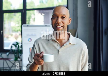 Chronische Krankheit, Inklusion, kühner afroamerikanischer Mann mit Myasthenia gravis Krankheit halten eine Tasse Kaffee, glücklich und dunkel gehäutete Büroangestellte mit Stockfoto