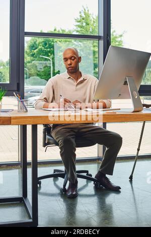 Inklusion, afroamerikanischer Mann mit Myasthenie bei der Arbeit, kühner und dunkelhäutiger Büroangestellter, Unternehmenskultur, Monitor und Smartphone, Computer-anonym Stockfoto