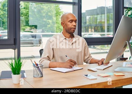 afroamerikanischer Mann mit Myasthenie-Störung bei der Arbeit, kühner und dunkelhäutiger Büroangestellter, Inklusion, Unternehmenskultur, Monitor und Smartphone, COMP Stockfoto