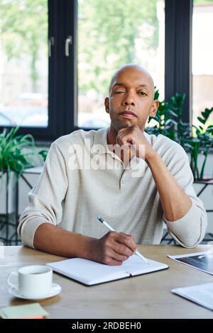 Professionelle Kopfaufnahmen, Mann mit Ptosis, der Notizen macht, kühner afroamerikanischer Geschäftsmann, der in die Kamera schaut, dunkelhäutiger Büroangestellter mit Myasthenie Stockfoto